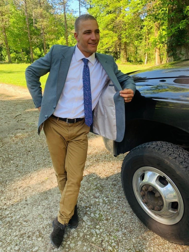 young man wearing suit and khakis leaning on truck